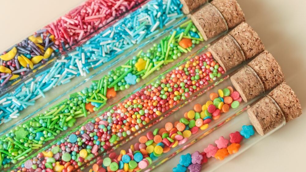 6 Reagenzgläser mit Korken von oben schräg, gefüllt mit bunten Zuckerperlen und Streuseln