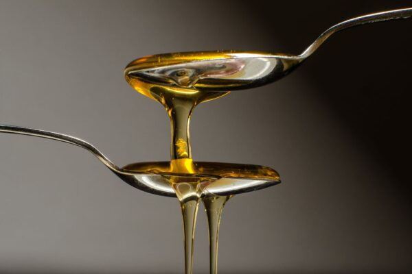 Deux cuillères pleines de miel tenues l'une sur l'autre. Le miel s'écoule par-dessus les cuillères en bas de l'image.