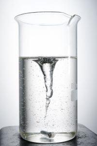 Ein Becherglas, halb voll mit Flüssigkeit, die in der Mitte einen Tornado bildet, weißer Hintergrund