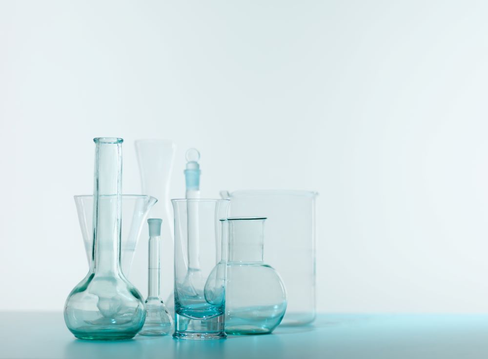 Sur le côté gauche de l'image se trouvent plusieurs verres de laboratoire vides, sur un fond légèrement bleuté.